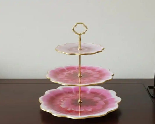 Three-tiered cake stand with pink floral design on a wooden surface, 